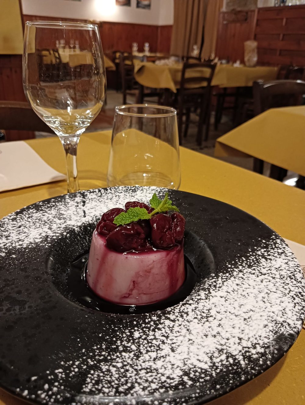 Bianco mangiare con visciole e menta su un piatto nero spolverato di zucchero a velo